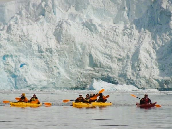 Kajakfahrer vor einer riesigen Eiswand in der Antarktis.