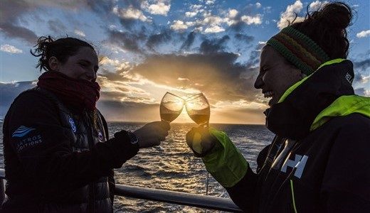 Zwei Frauen in Albatros Jacken stoßen vor dem Sonnenuntergang mit den Gläsern an.