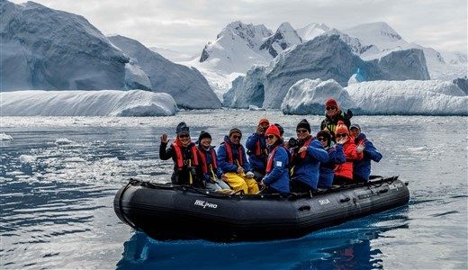 Gruppe von Gästen sitzt auf dem Zodiac, im Hintergrund Eisberge