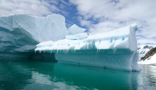 Blaugrün schimmert das Wasser der Antarktis um einen Eisberg